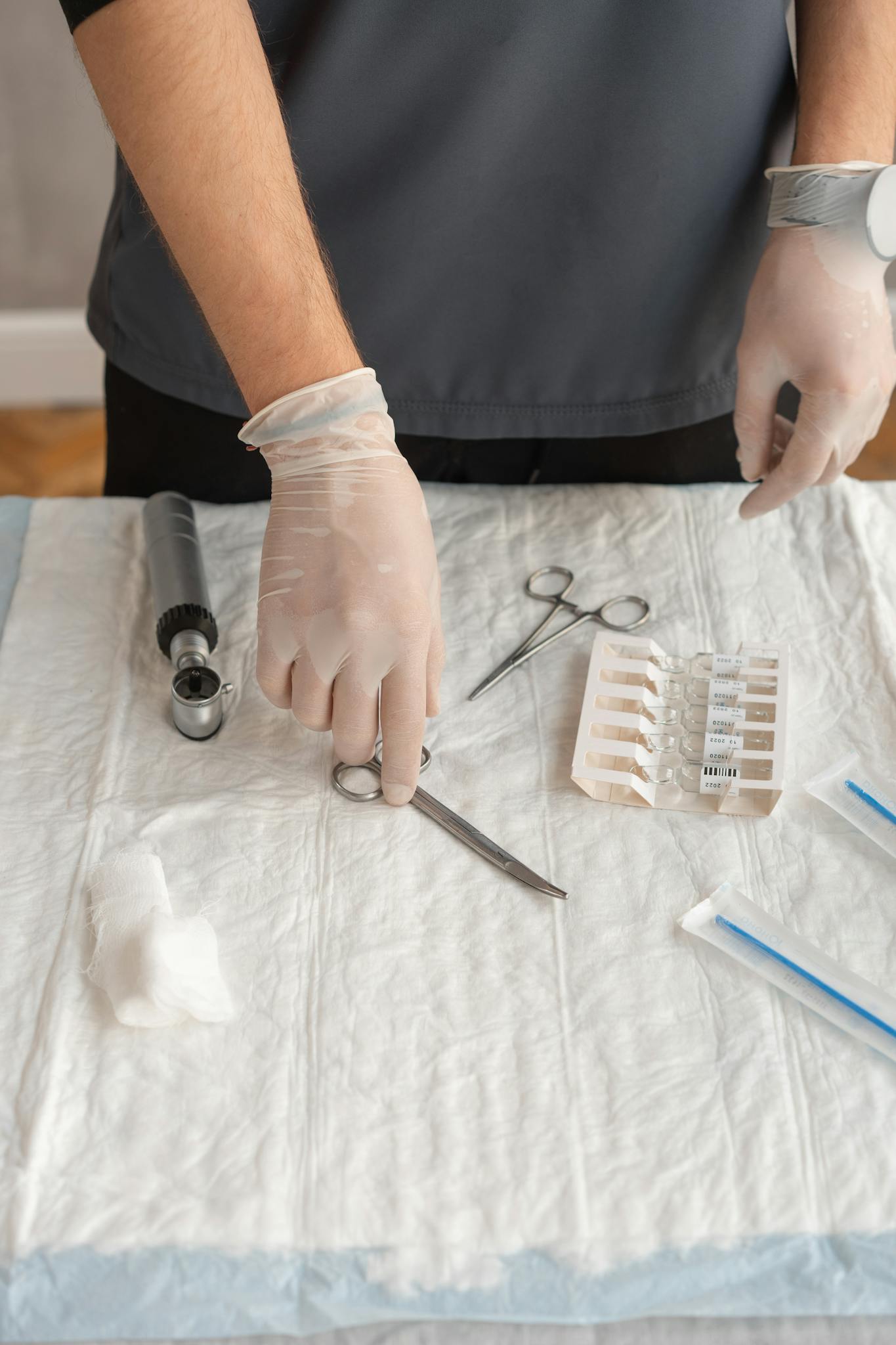 A healthcare professional wearing gloves preparing medical instruments on a sterile surface.