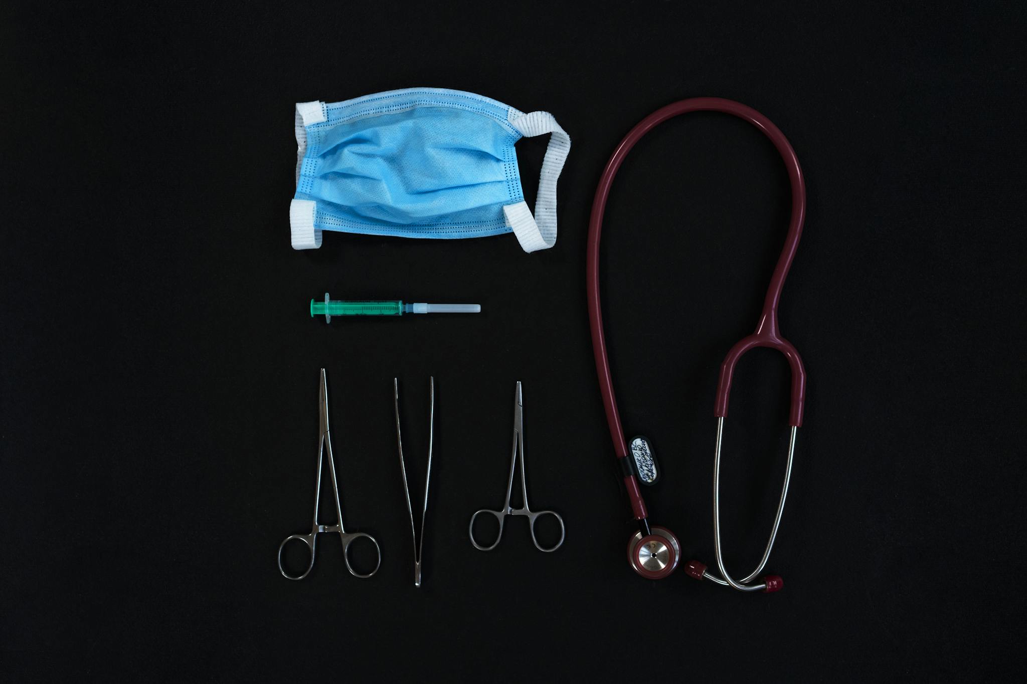 Top view of medical tools including a mask, syringe, and stethoscope on a black surface.